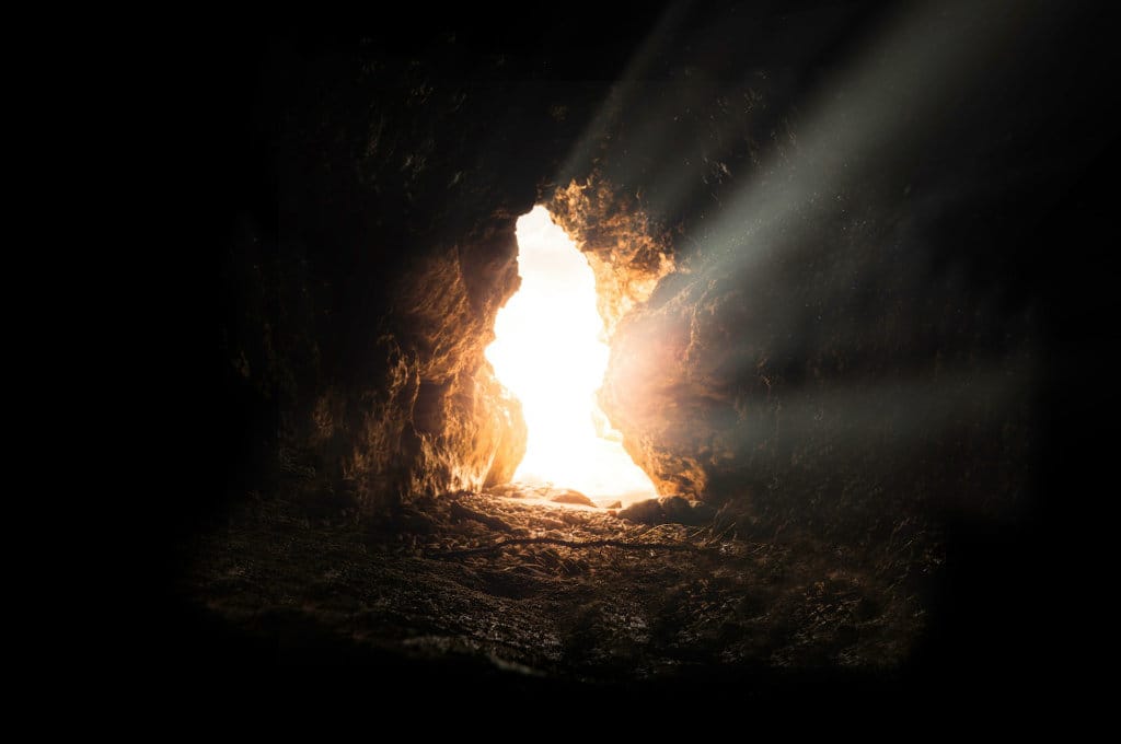 Sun rays beaming into an empty stone cave for a post about what makes Jesus different